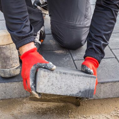 Hands of worker installing concrete paver blocks with rubber ham - Turnkey Paver Patios